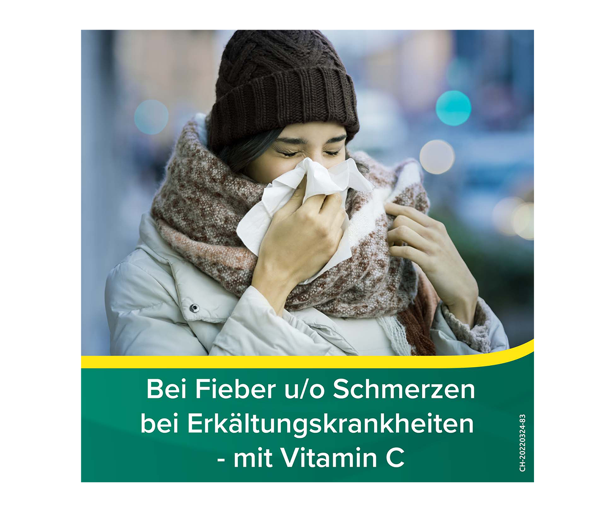 Frau mit Schal, Mütze und dicker Jacke welche ihre Nase putzt; Titel: Bei Fieber u/o Schmerzen bei Erkältungskrankheiten - mit Vitamin C