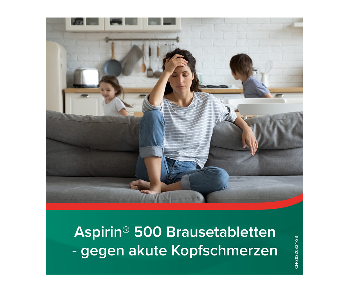 Frau auf einem Sofa die sich an den Kopf fasst mit spielenden Kindern im Hintergrund. Titel: Aspirin 500 Brausetabletten - gegen akute Kopfschmerzen 